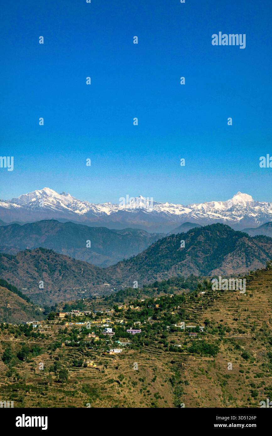 A breathtaking view of the Himalayas with snow-covered peaks shining under a clear blue sky. The green hills, winding road, and small temple add beauty, peace, and adventure to this stunning mountain landscape. - Smartphone Captured Stock Image