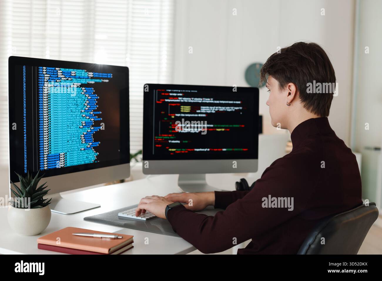 Programmer working on computer with dual monitors at white table in office Stock Photo