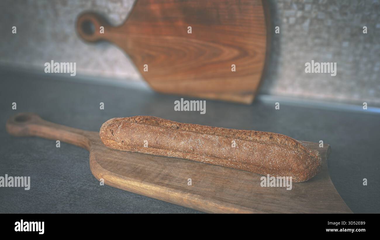 Long dark brown baguette on a rustic wooden board placed on a table, top-down shot for bakery and food advertising use Stock Photo