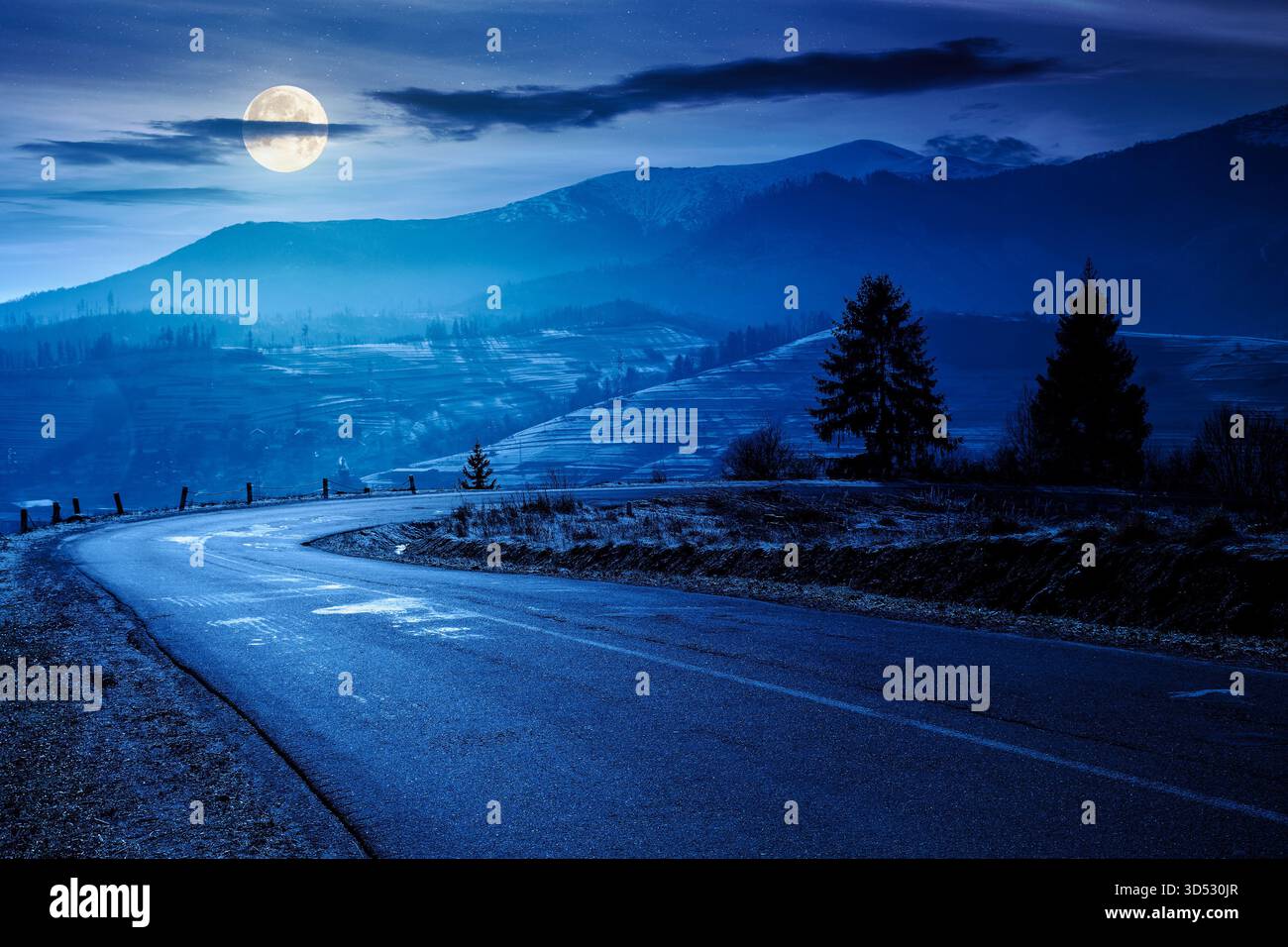 country road in mountains at night. beautiful countryside landscape in late autumn. fir trees on the roadside in full moon light. scenic view of blue Stock Photo