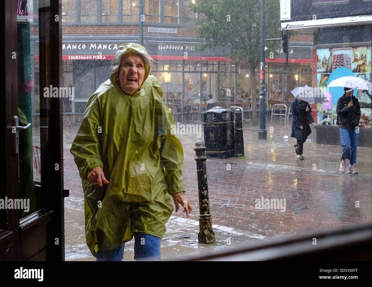 An elderly lady grimaces as she runs from  the torrential rains in Canterbury Kent 13/11/2025 Stock Photo