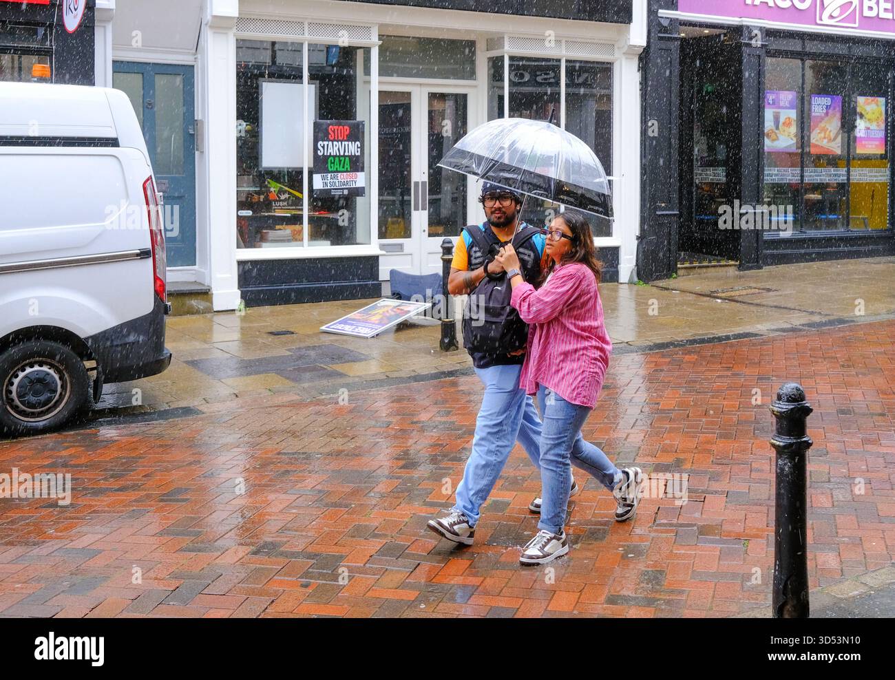 A couple use a small seethru umbrella during heavy rain.  Canterbury Kent 13/11/2025 Stock Photo