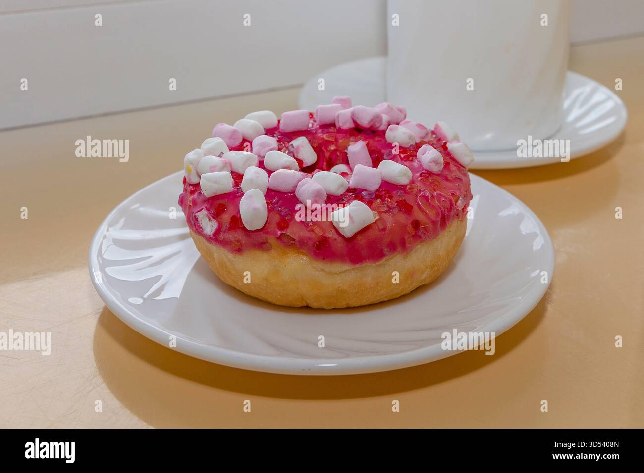 Pink glazed donut with marshmallows on white plate near ceramic coffee cup Stock Photo