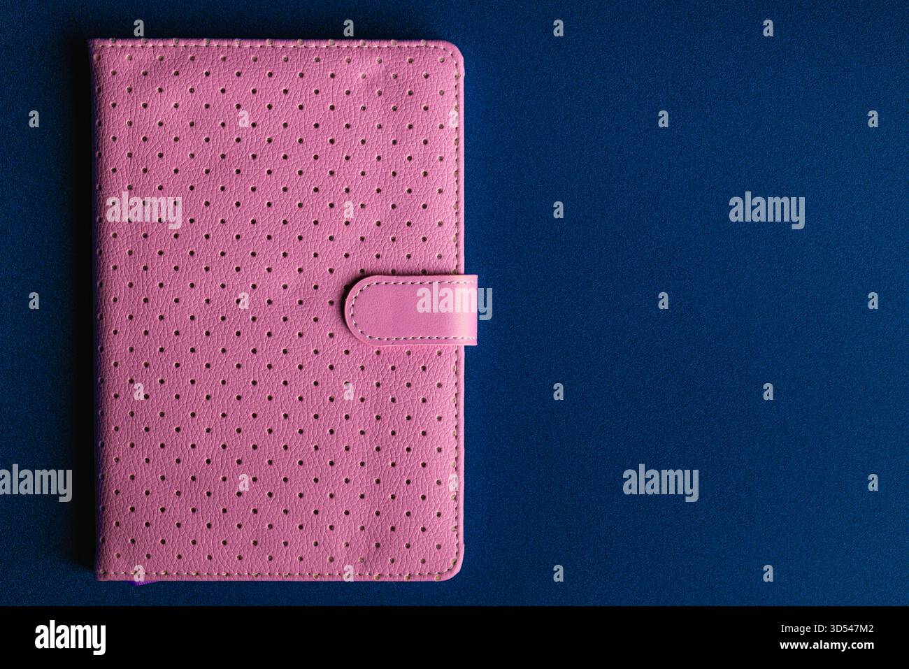 Overhead View of Closed Pink Perforated Notebook on Dark Blue Background Stock Photo