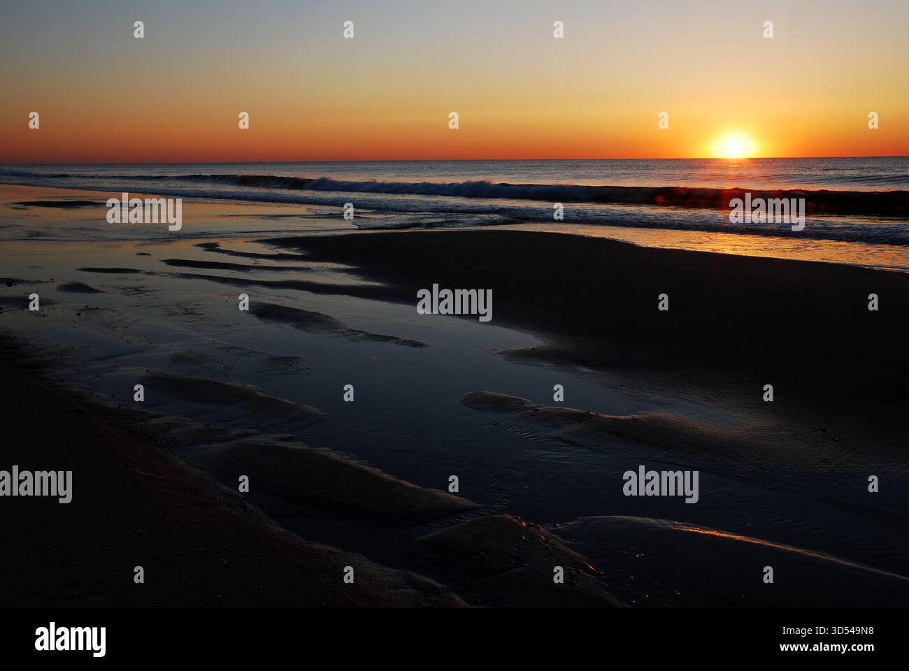 Ripples in the sand reflect the early morning light of a rising sun on ...