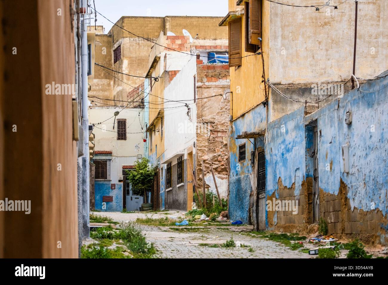 Rabat, Morocco – A narrow alley in an old residential neighborhood featuring weathered buildings painted in blue, yellow, and white. Stock Photo
