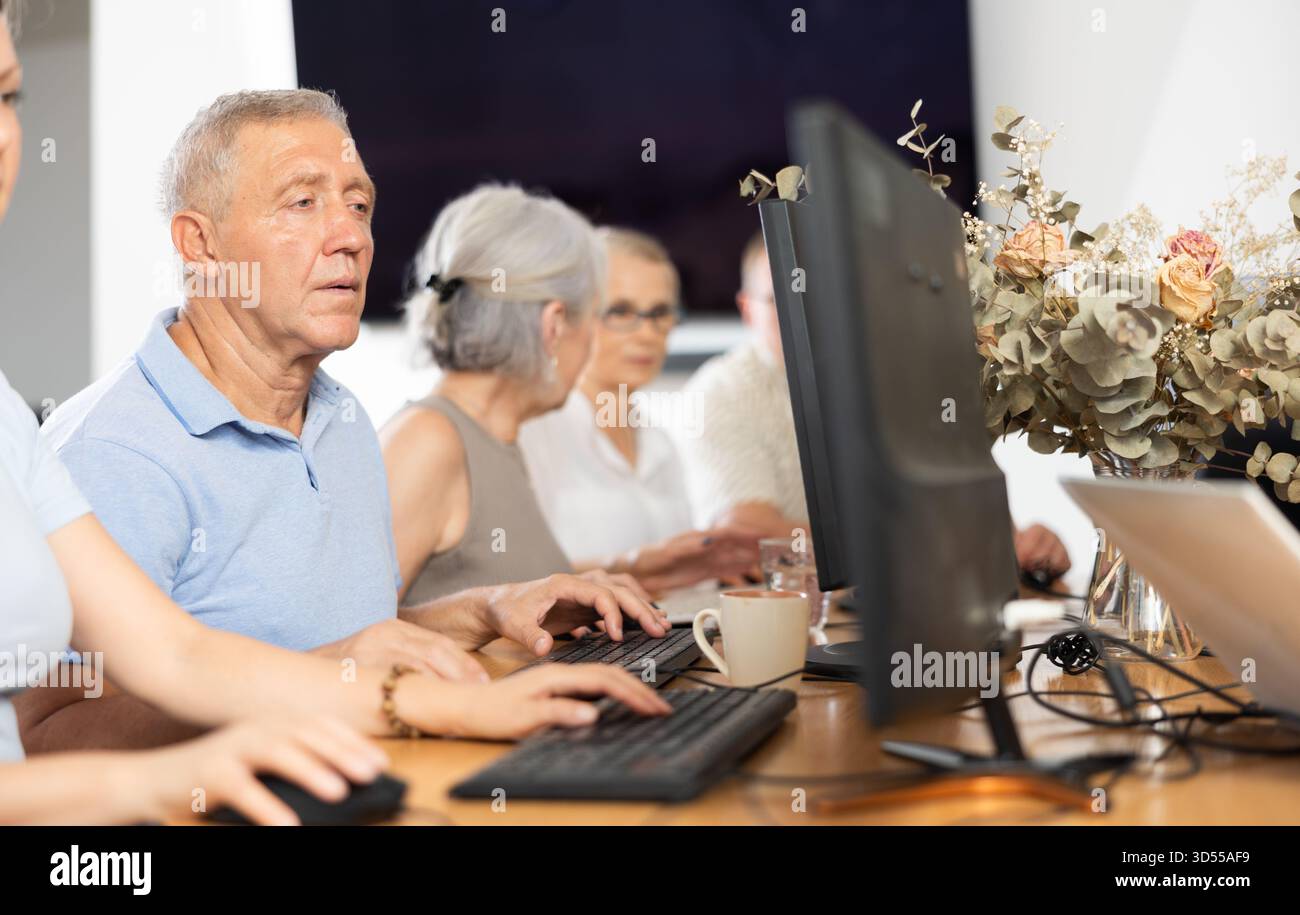Concentrated elderly man immersed in using computer in library Stock Photo