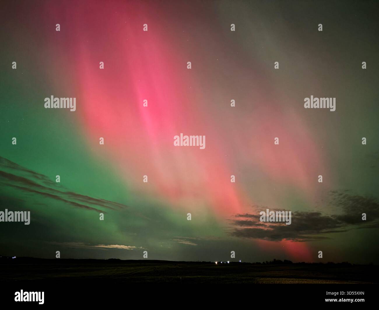 Vibrant northern lights with green and pink hues illuminate a dark prairie sky above a flat landscape and road at night. - Smartphone Captured Stock Image