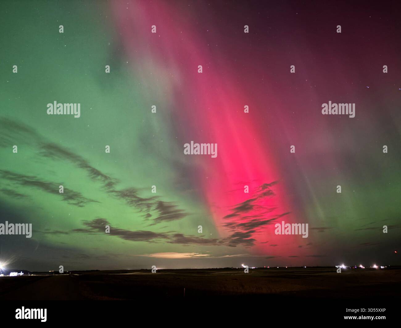 Vibrant northern lights with green and pink hues illuminate a dark prairie sky above a flat landscape and road at night. - Smartphone Captured Stock Image