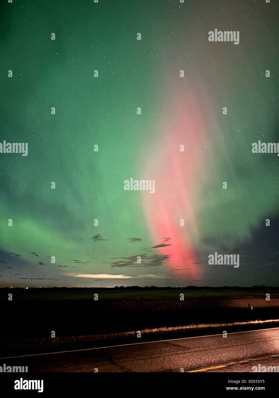 Vibrant northern lights with green and pink hues illuminate a dark prairie sky above a flat landscape and road at night. - Smartphone Captured Stock Image