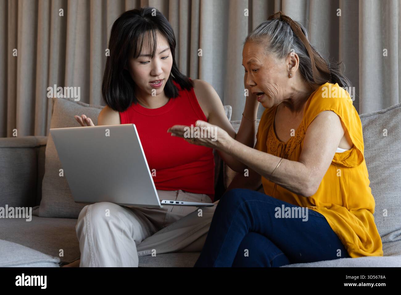 Asian women discussing something on laptop while sitting on sofa at home Stock Photo
