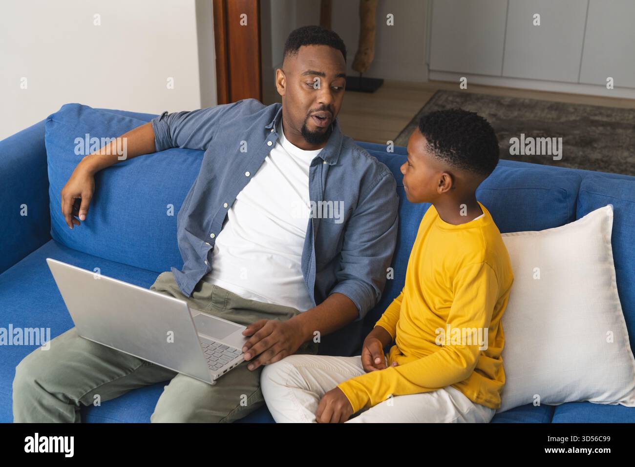 Father and son talking on sofa while using laptop at home Stock Photo