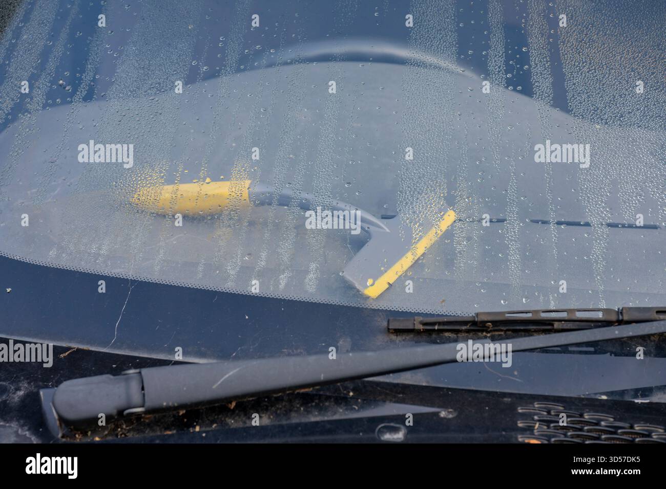 Car windscreen and dashboard with condensation build up and ice scraper squeegee on top of dashboard or steering column for demisting or defogging win. Stock Photo