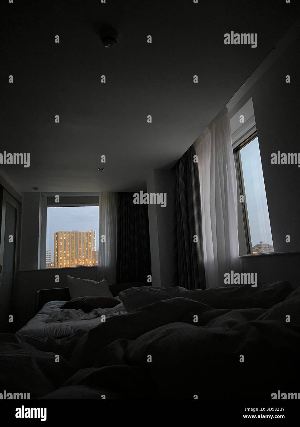 A low-light hotel room scene featuring a window overlooking a city building in Leeds, England. The moody lighting creates a peaceful, reflective atmos - Smartphone Captured Stock Image