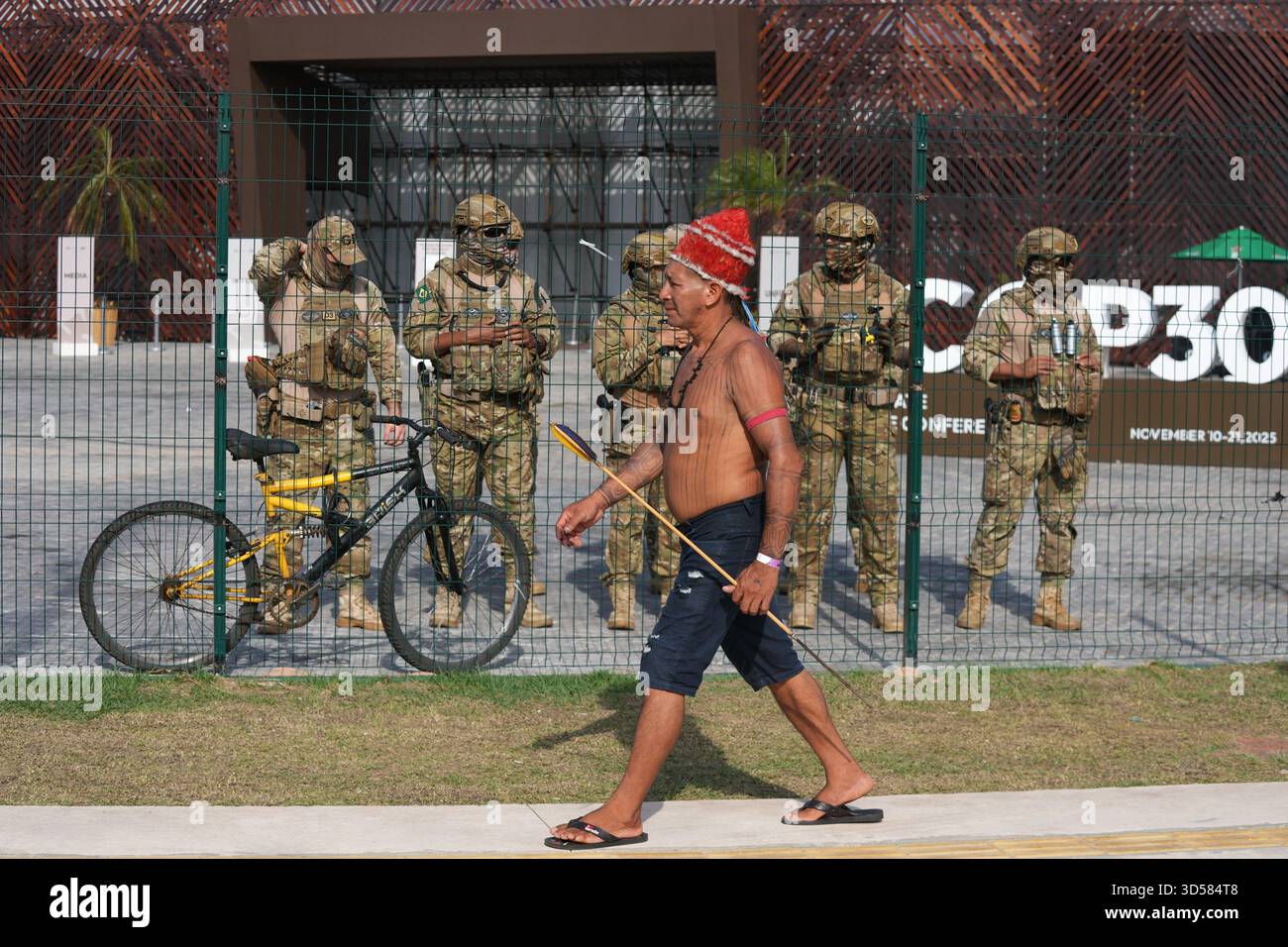 An Indigenous man walks past a group of security personnel near a fence ...
