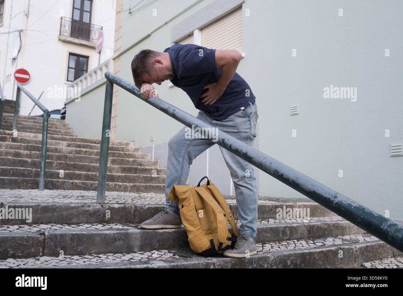 A Young Man Having a Heart Attack on the Street, Standing on the Stairs and Holding His Chest  Stock Photo