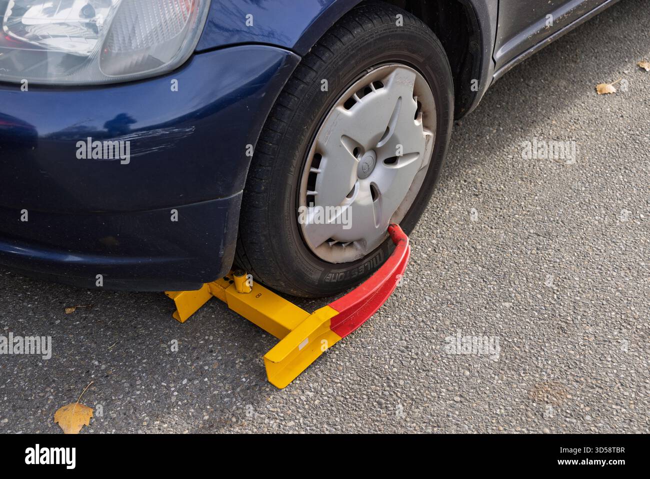 A blue car with a bright yellow and red wheel clamp, or immobilizer, fitted to the front tire, a common method for enforcing parking fines. Utrecht Ne Stock Photo