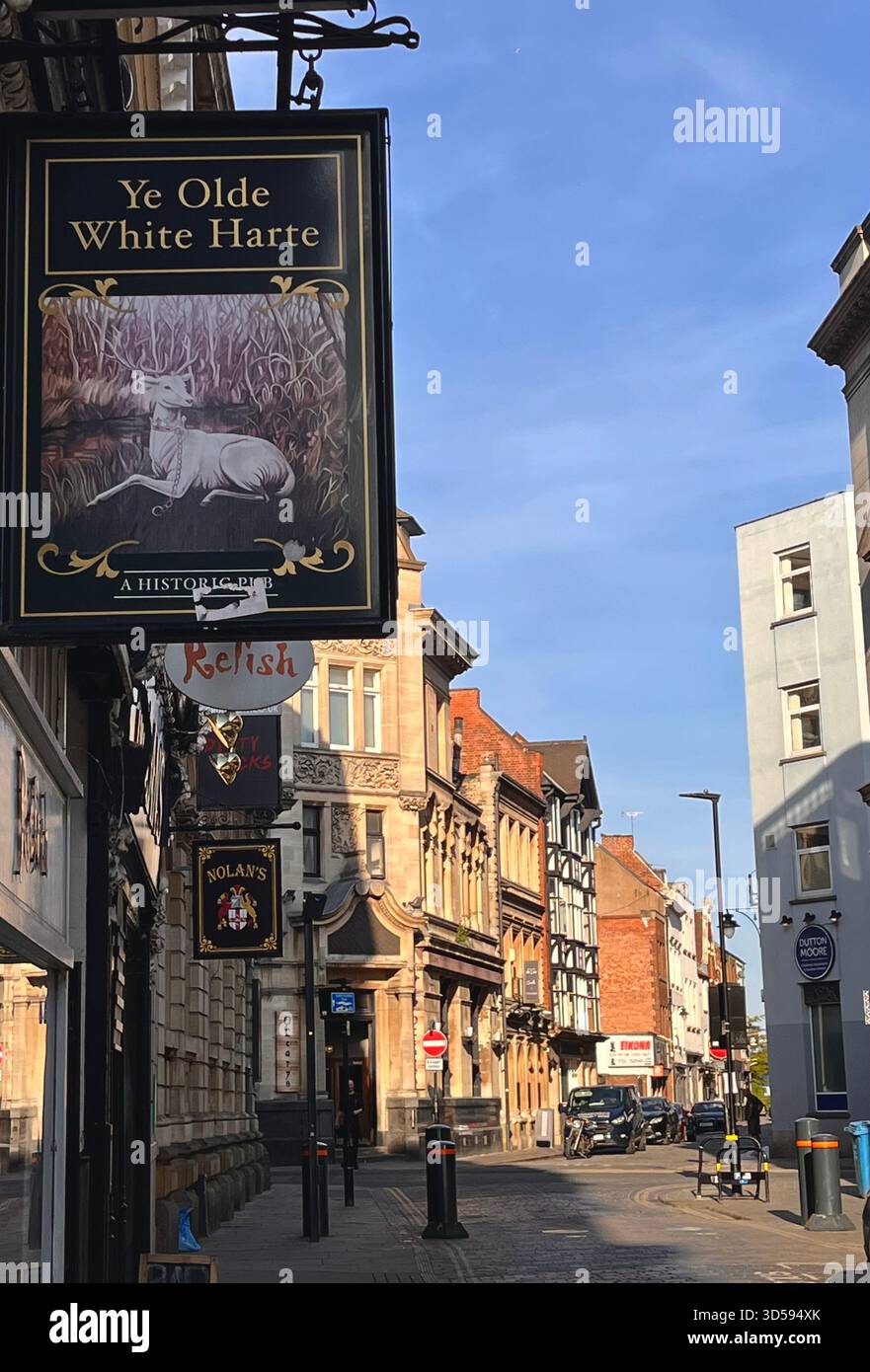 A lively historic street in Hull, England, featuring the classic hanging sign of Ye Olde White Harte. The warm architecture, pedestrians, and bright d - Smartphone Captured Stock Image