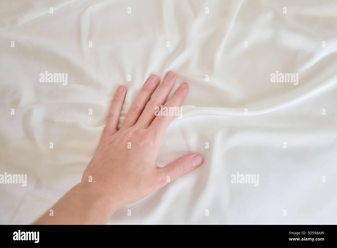 Female hand gently touching white silky sheet Stock Photo