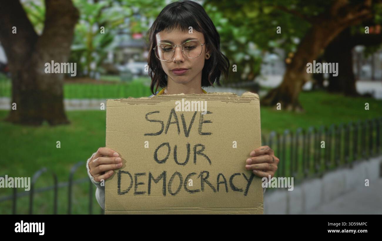 Resolute Sign Woman holds protest sign reading save our democracy in a lush green ...