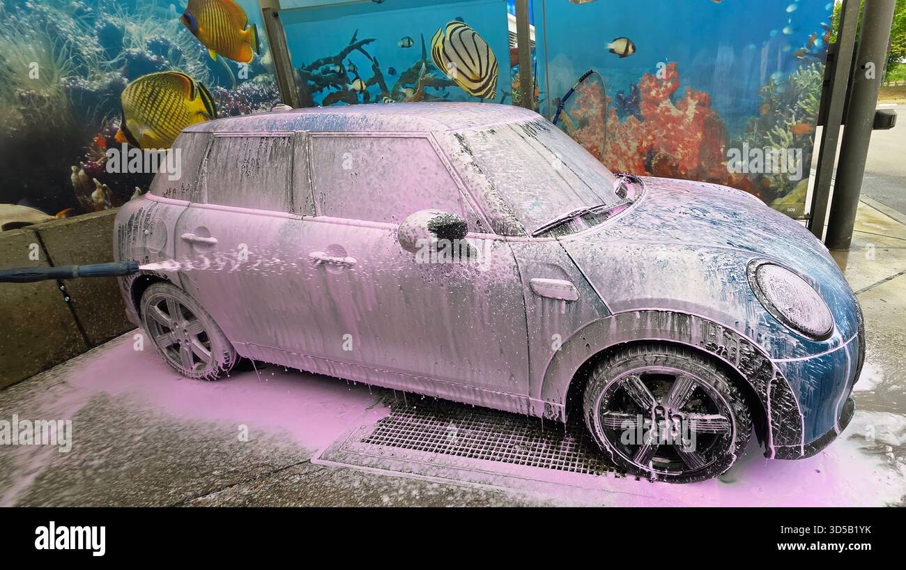 Berlin, Germany - May 18, 2025: Mini Cooper is being washed with foam at a car wash featuring an underwater mural. - Smartphone Captured Stock Image