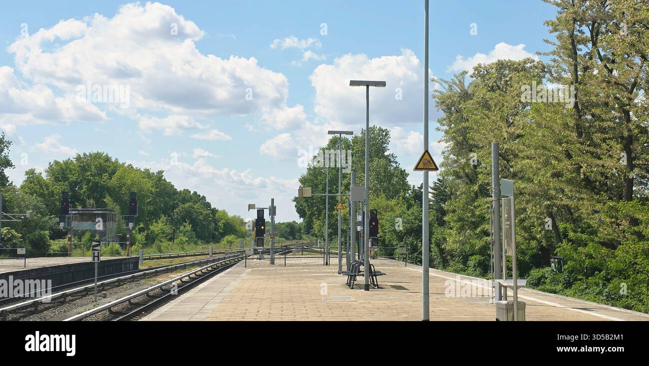 Berlin, Germany - May 26, 2025: Train station platform features trees and blue sky under bright sunlight. - Smartphone Captured Stock Image