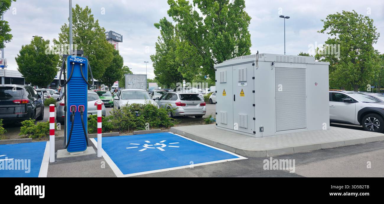 Berlin, Germany - June 28, 2025: Electric vehicle charging station features power unit in busy parking lot surrounded by trees. - Smartphone Captured Stock Image