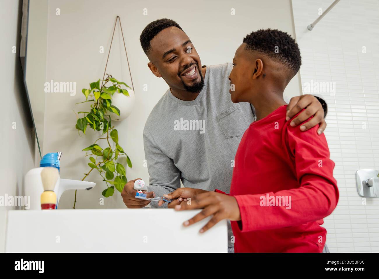 African American African American father helping son brush teeth in bathroom, both smiling warmly Stock Photo