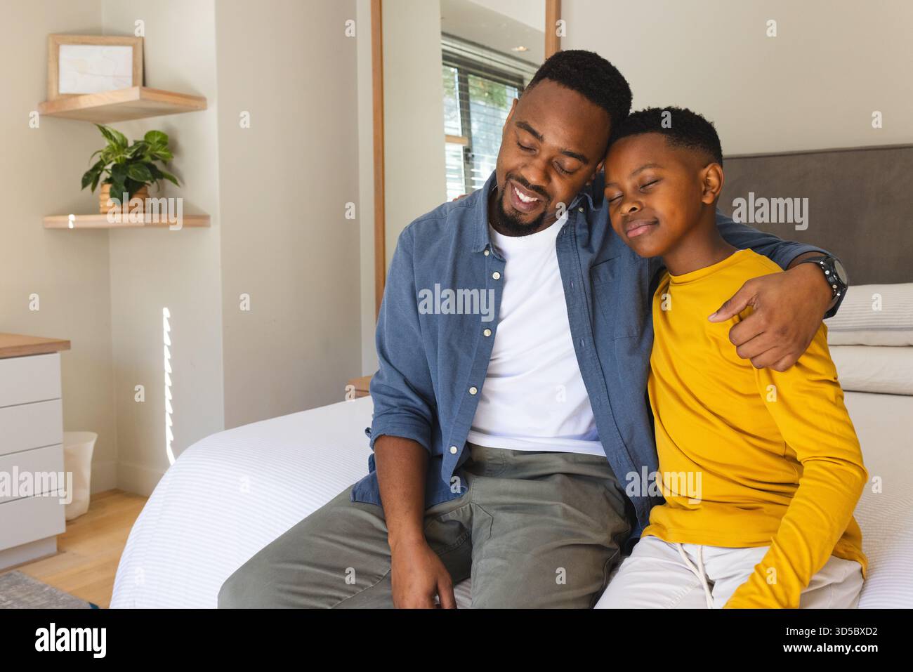 Father and son sitting on bed, embracing and smiling at home Stock Photo