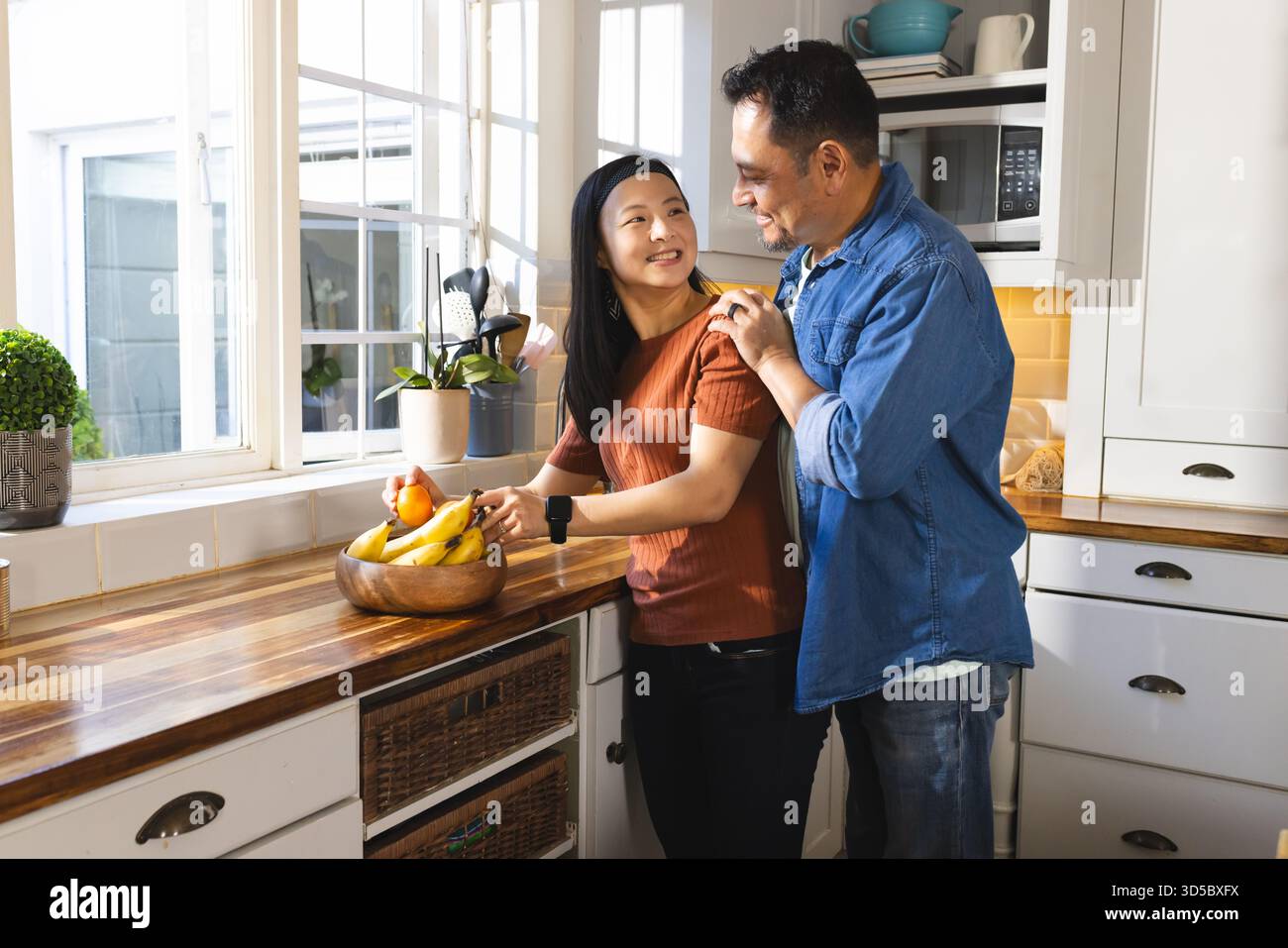 Asian couple in kitchen sharing affectionate moment while preparing fresh fruit Stock Photo