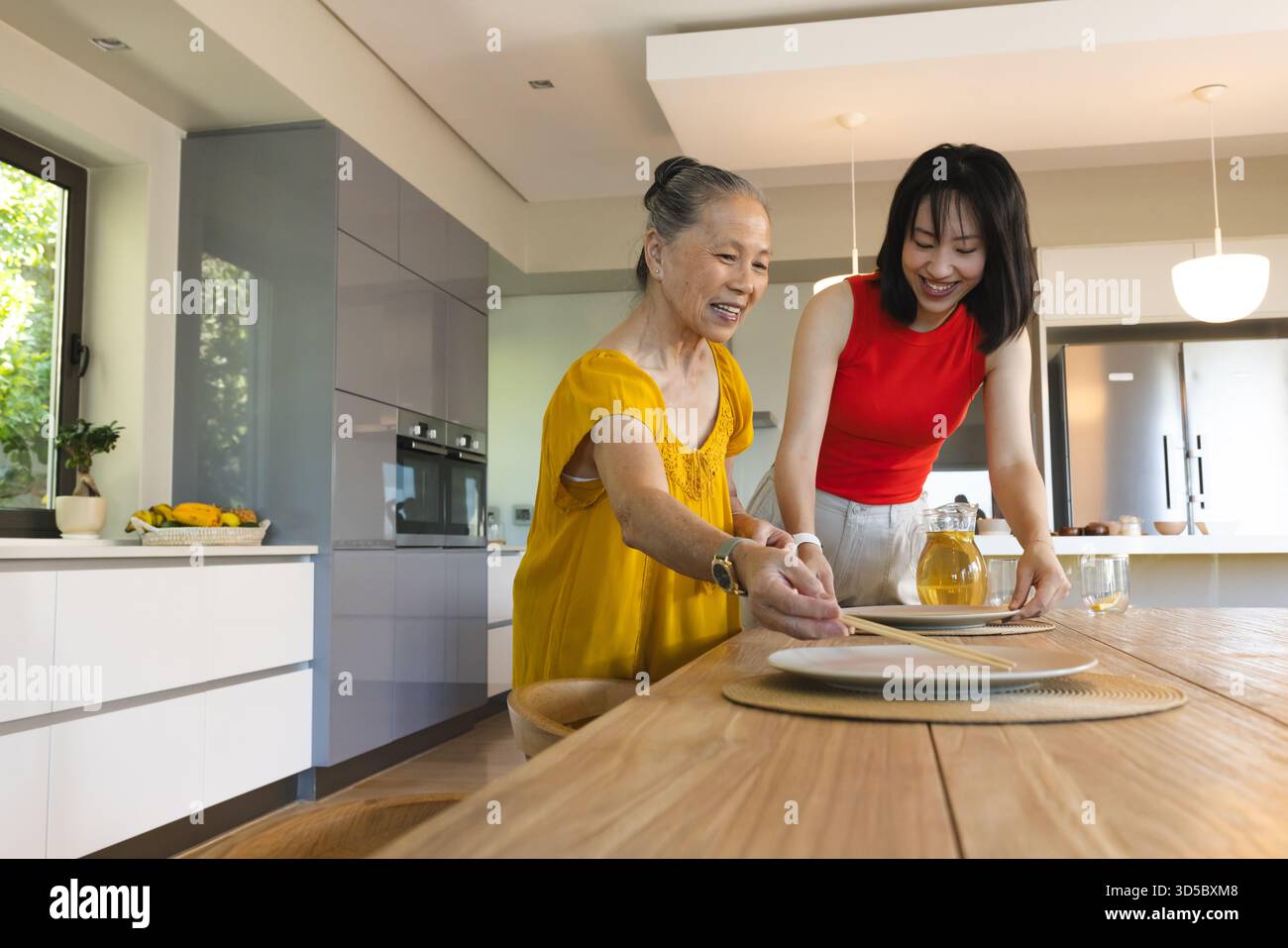 Asian senior mother and daughter setting dining table together, smiling ...