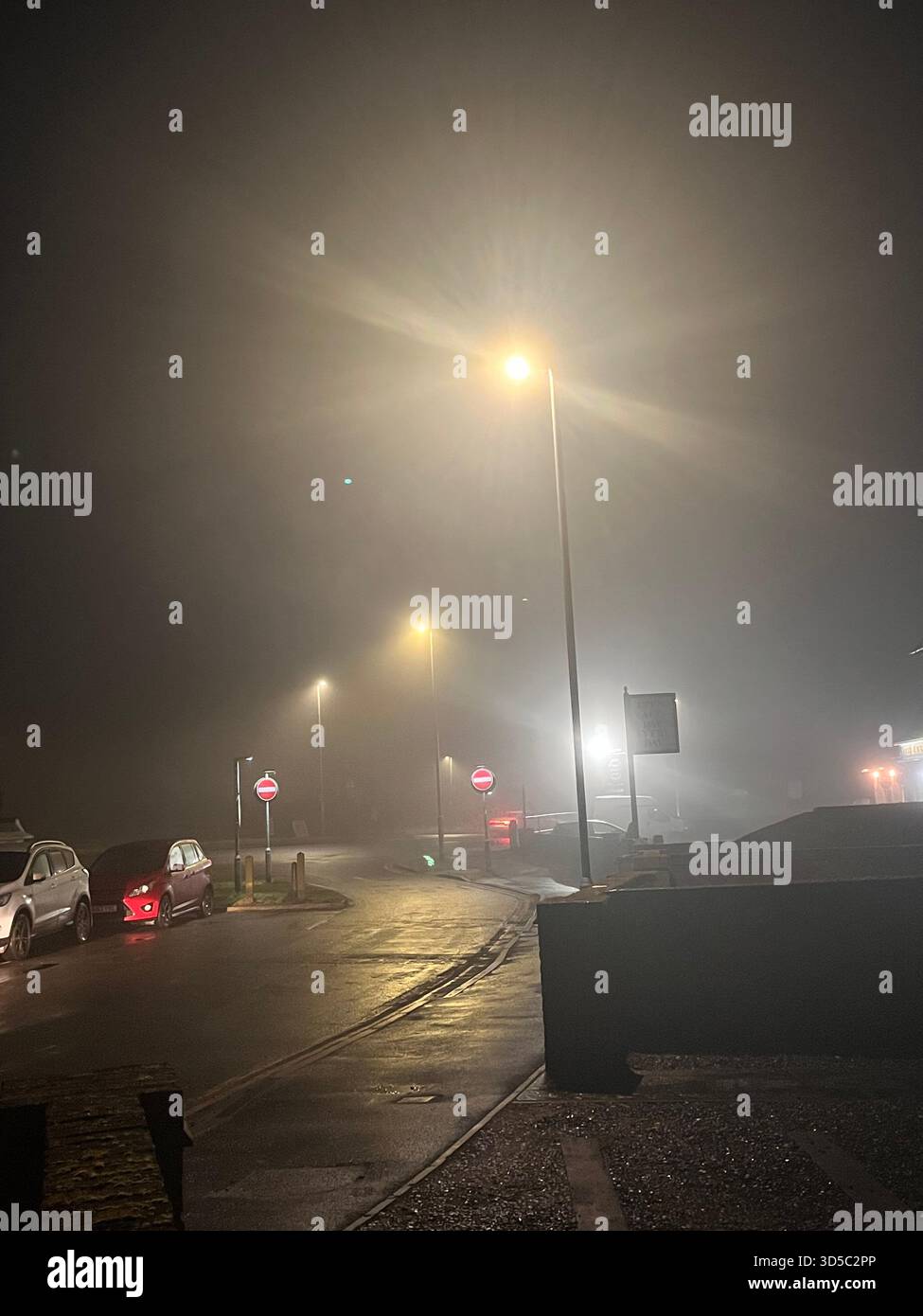 Nighttime urban scene with dense fog, bright streetlights and reflective wet asphalt on a quiet road in Hull, England. - Smartphone Captured Stock Image