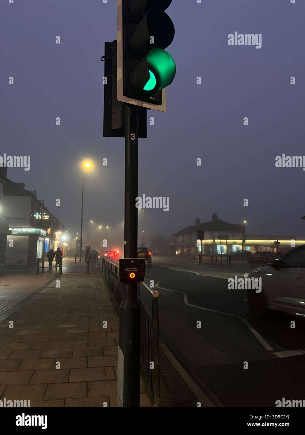 Green traffic light glowing through dense fog on a quiet urban street in Hull, England, with soft bokeh lights and misty early morning atmosphere. - Smartphone Captured Stock Image