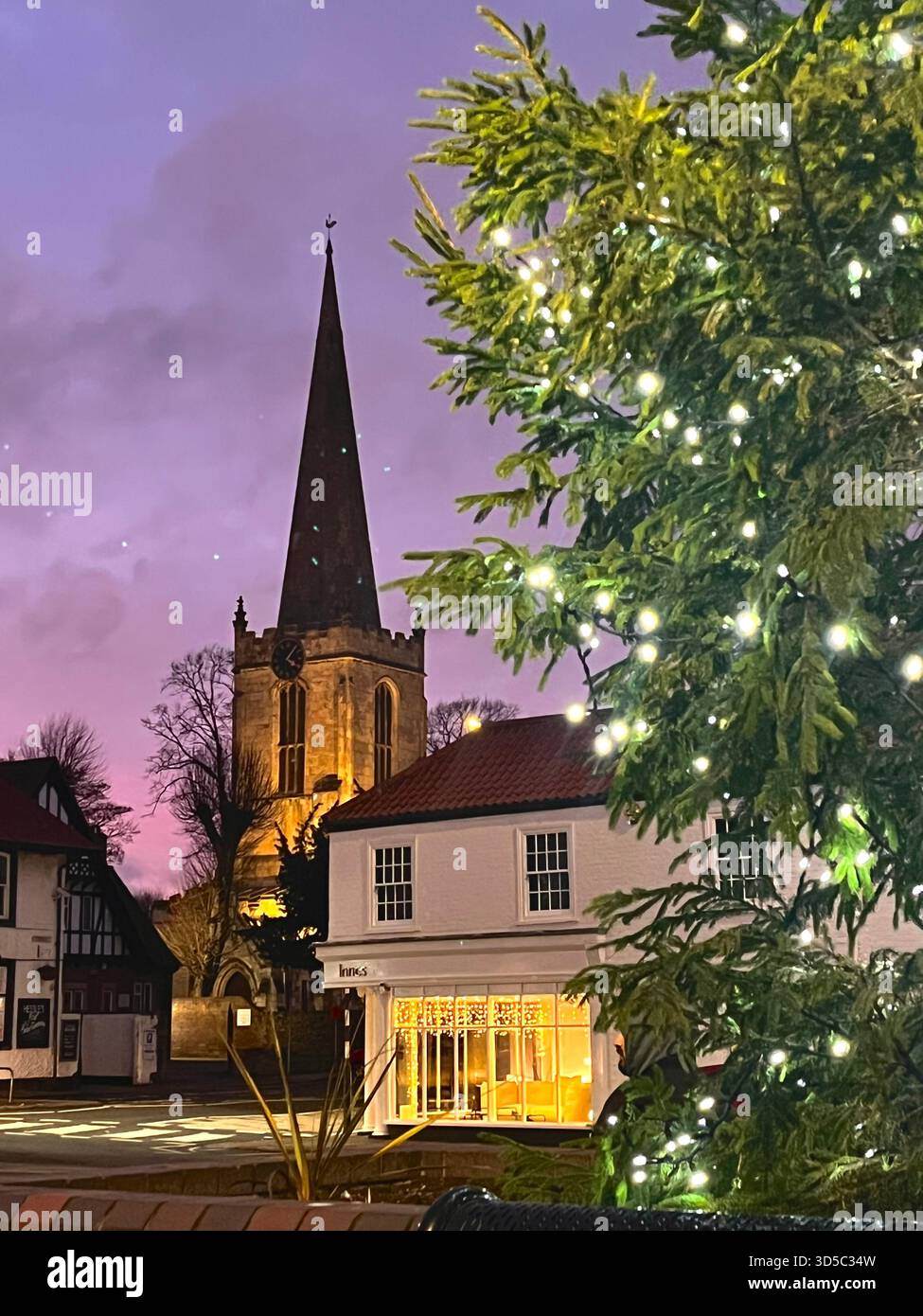 Historic church spire rising above rooftops at twilight with illuminated Christmas tree in the foreground in Hull, England, creating a festive winter - Smartphone Captured Stock Image