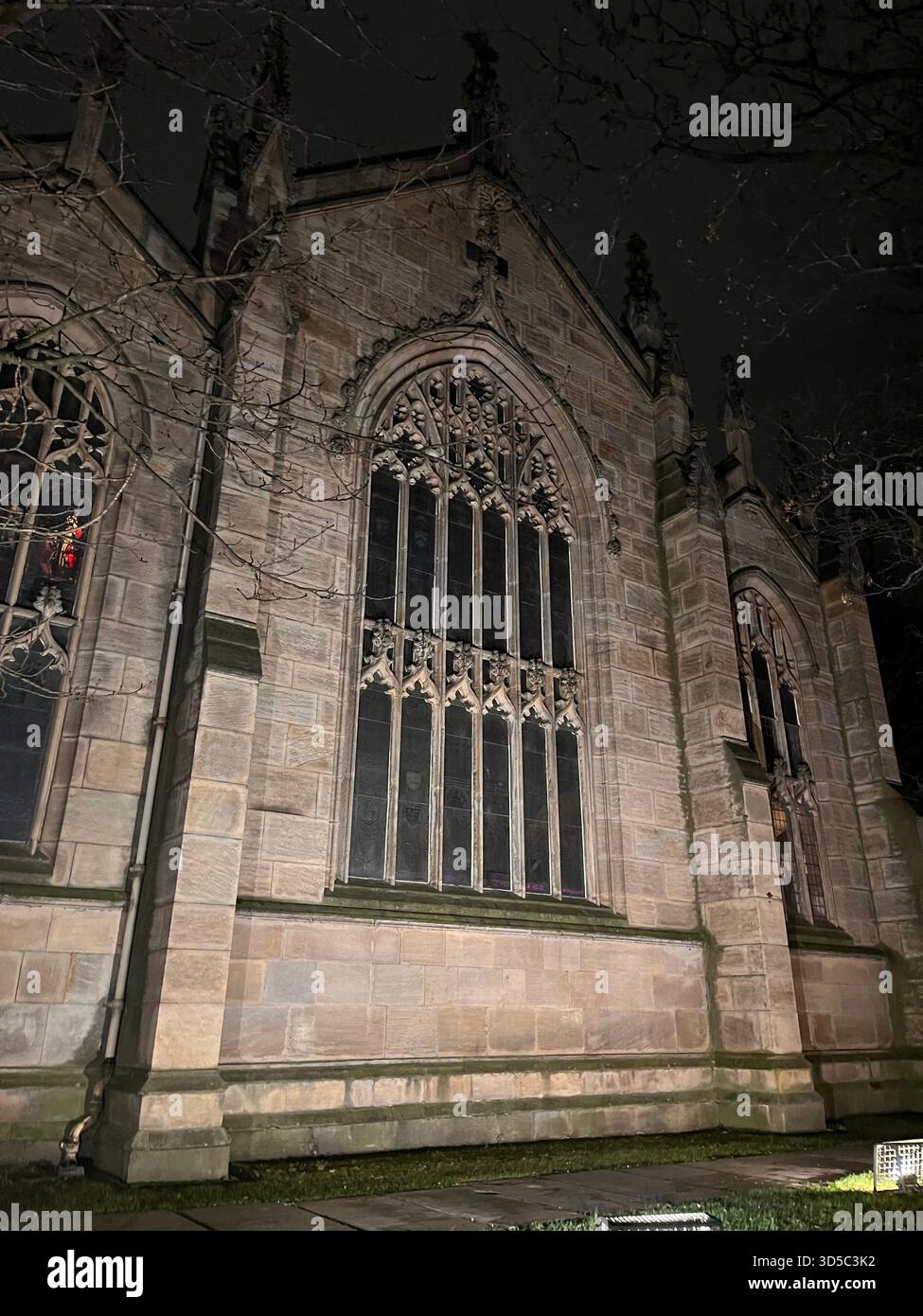 Close-up view of an illuminated Gothic church facade with tall arched windows and stone details at night in Leeds, England. - Smartphone Captured Stock Image