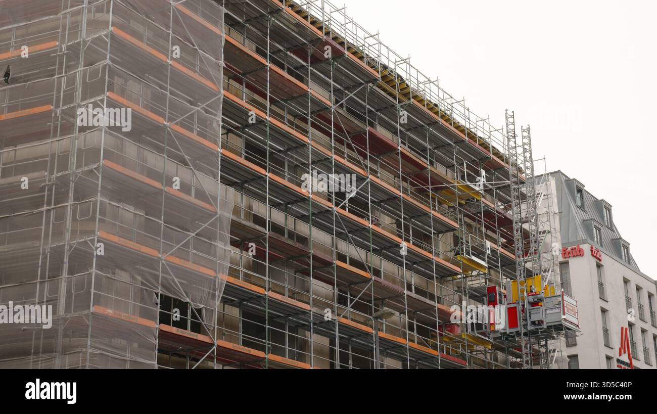 Workers are busy at a construction site, surrounded by scaffolding and machinery in a city area on a cloudy day. Stock Photo