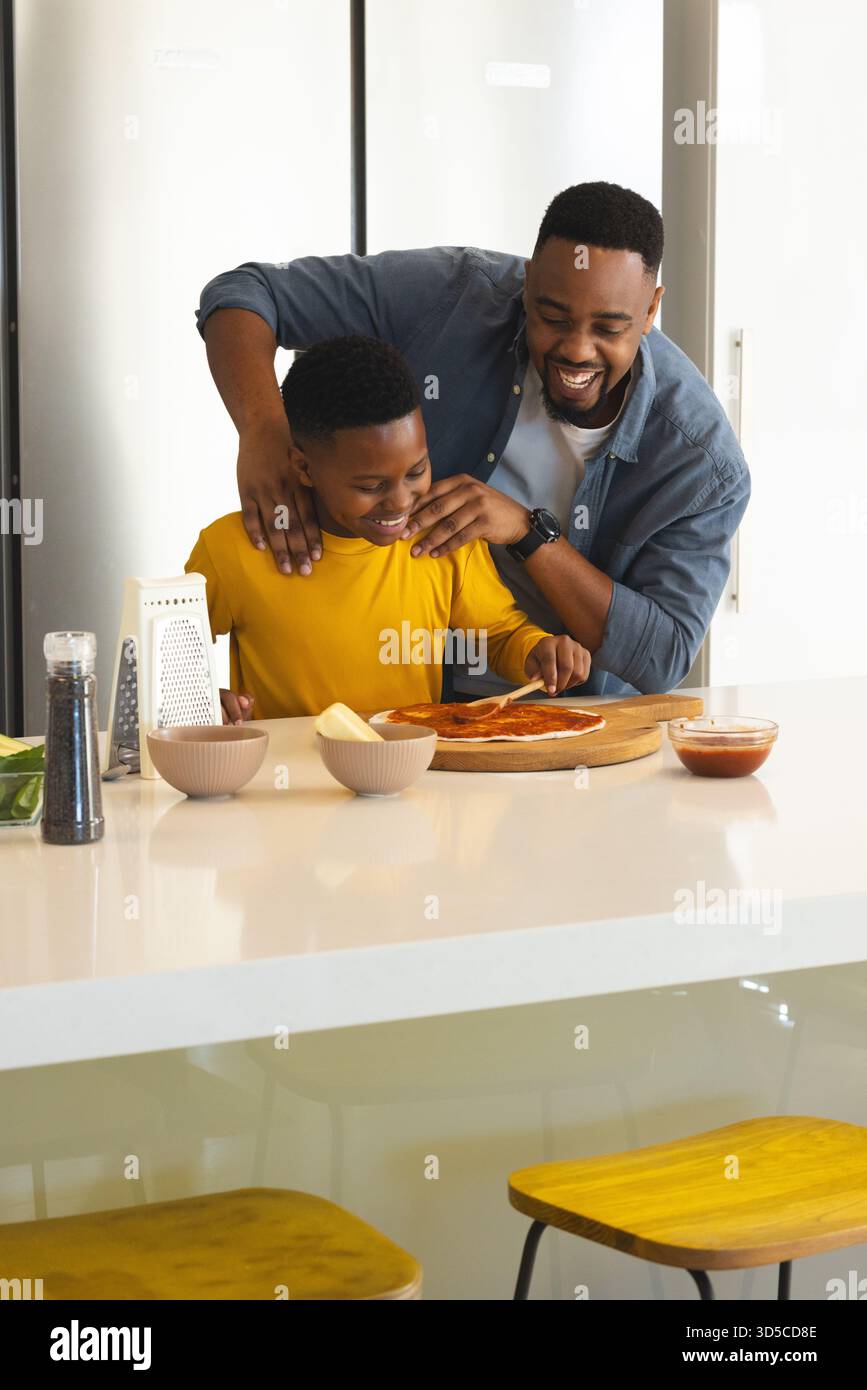 Father and son making pizza together in kitchen, sharing joyful moment Stock Photo