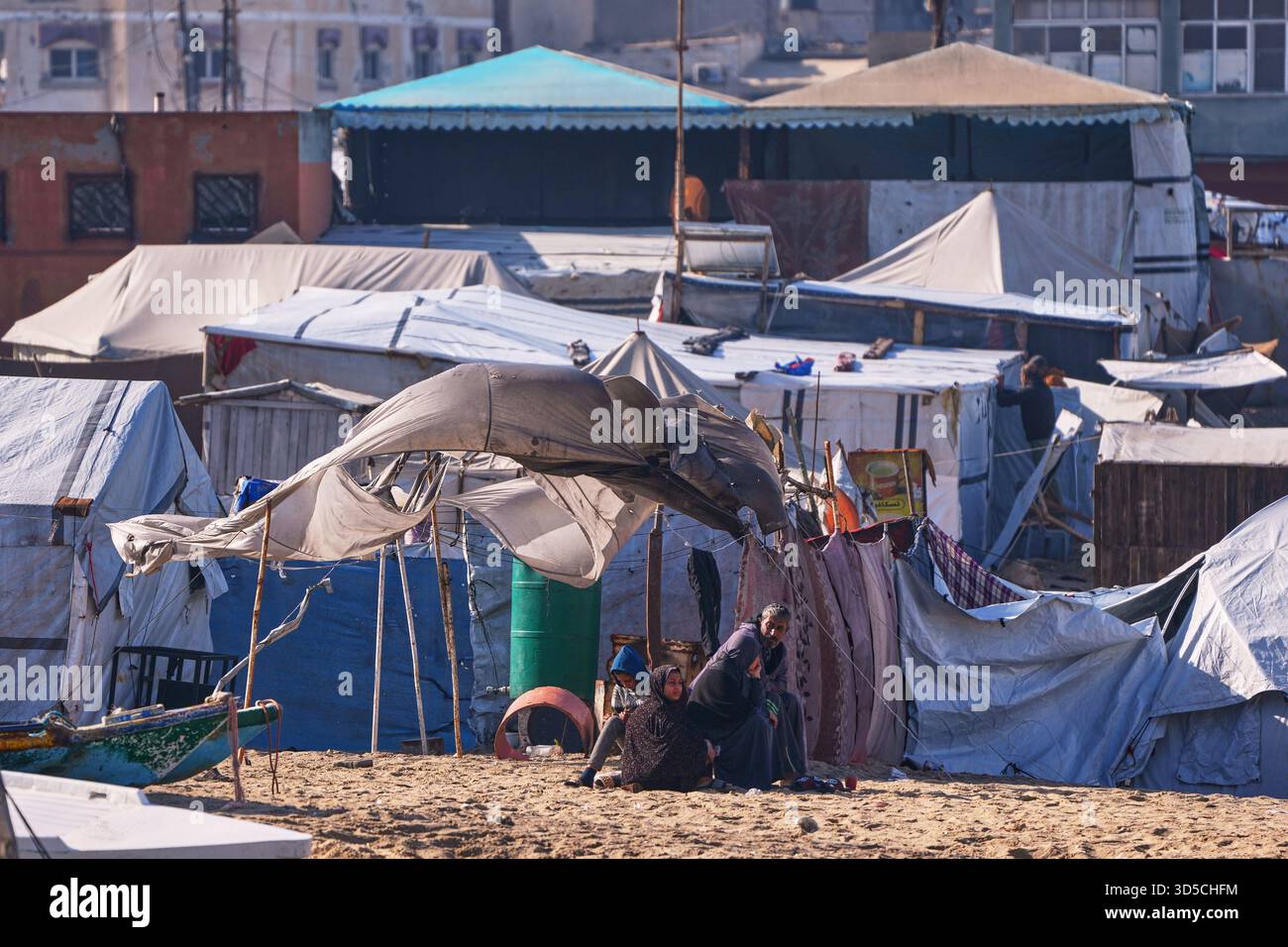 A displaced Palestinian family sits in front of their tent on the beach ...