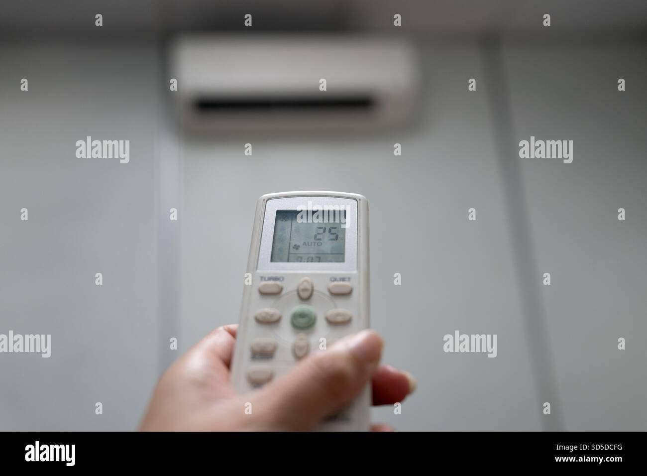 Hand Holding Air Conditioner Remote Control Set to 25 Degrees Celsius in AUTO Mode Stock Photo