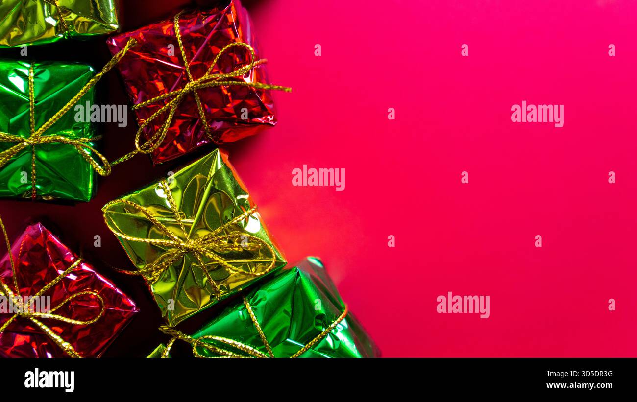 A shiny green, red, and gold wrapped gift boxes with gold strings sits against a red background. Christmas, holiday celebrations or sales events. Stock Photo