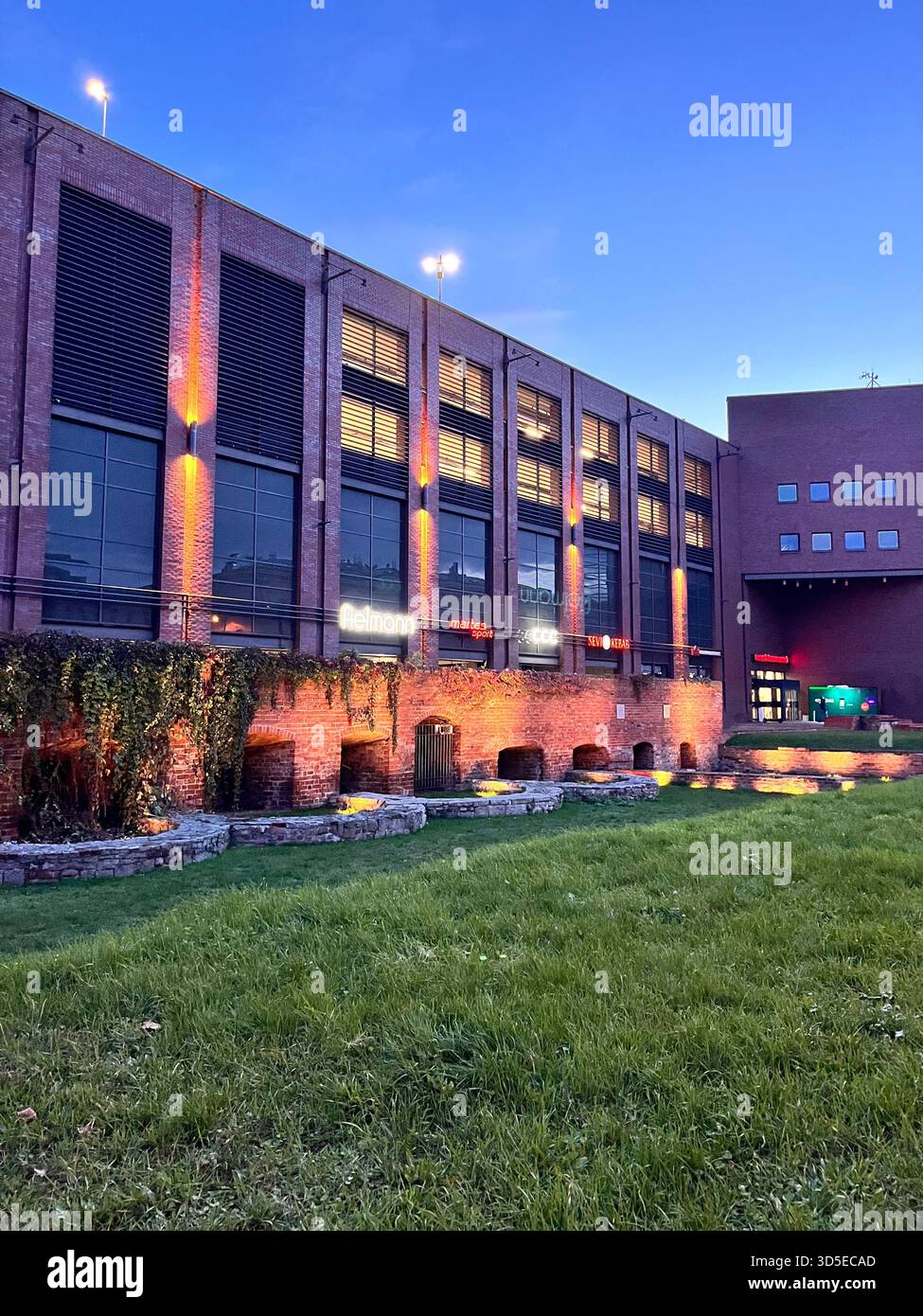 A contemporary brick building glowing with warm exterior lighting during dusk. Captured in Wrocław, Poland, the scene - Smartphone Captured Stock Image