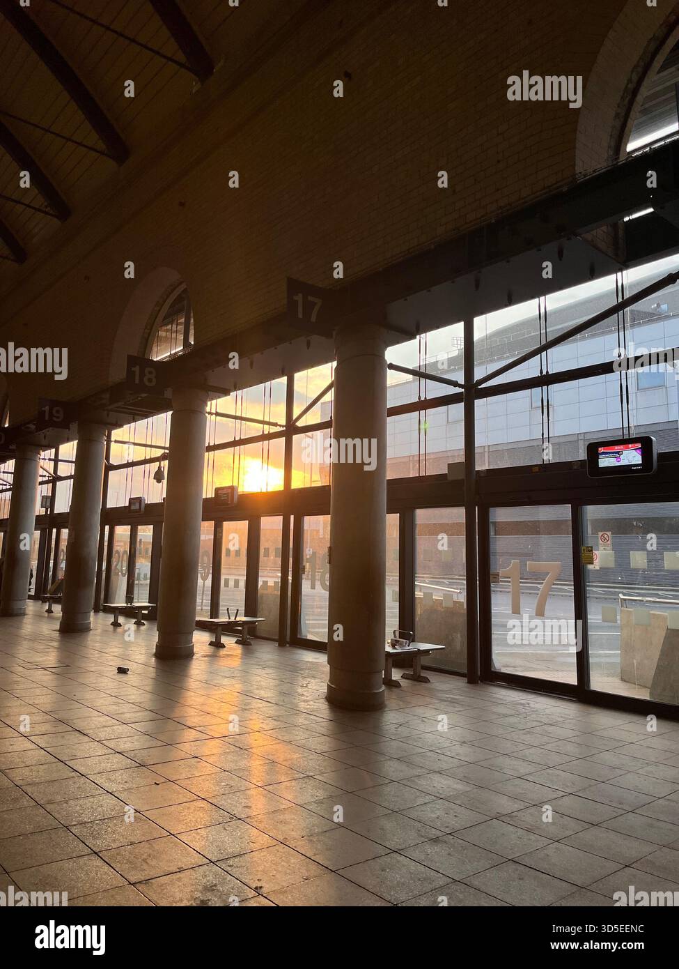 A warm sunset shines through tall glass windows inside a spacious station hall in Hull, England. - Smartphone Captured Stock Image