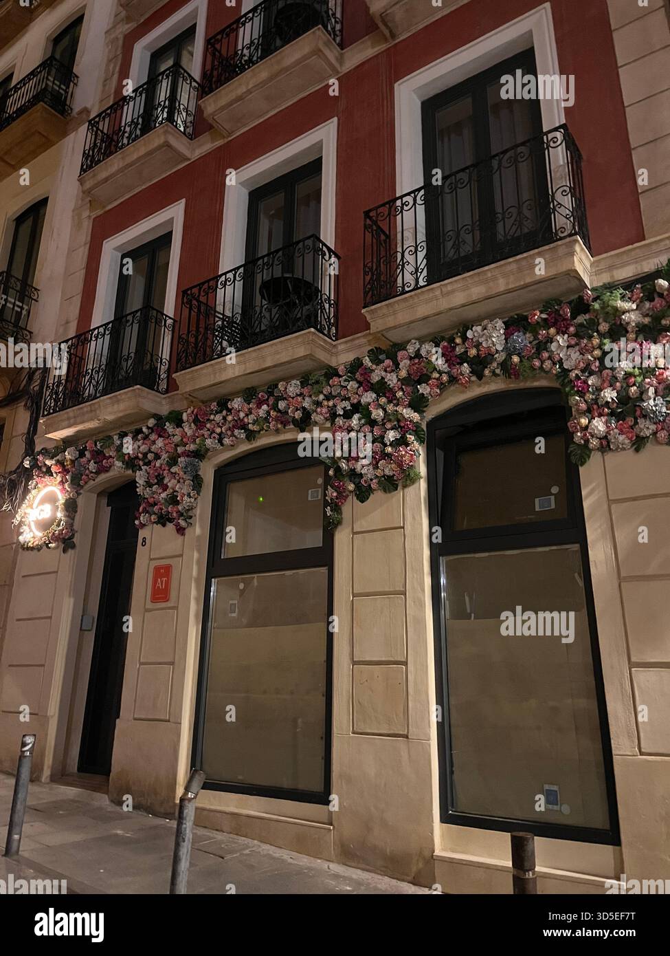 A charming facade in Alicante’s old town featuring a red-and-cream building with wrought-iron balconies and abundant floral decorations. - Smartphone Captured Stock Image