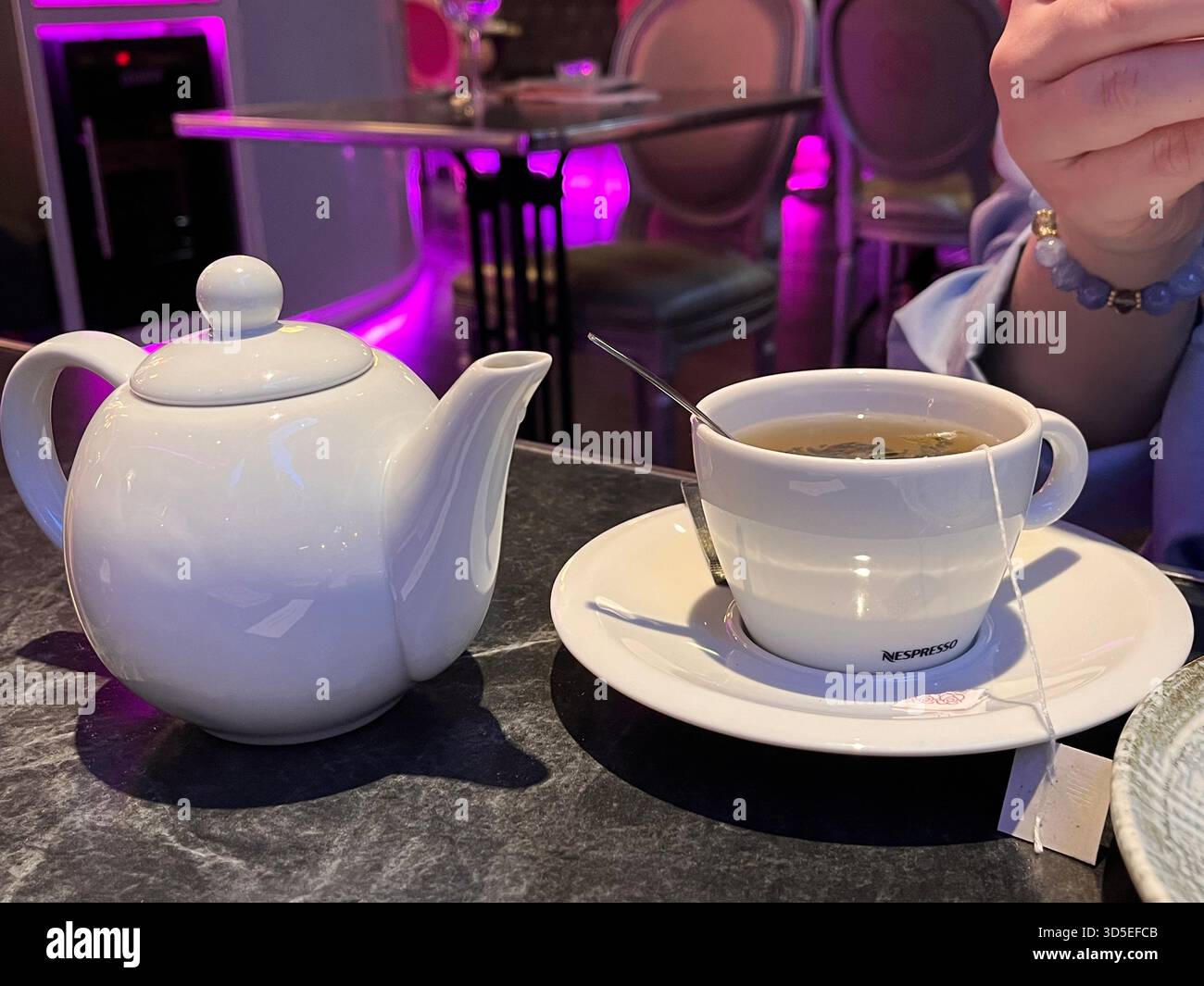 A warm and inviting café setting in Alicante featuring a white teapot, teacup, and saucer on a dark table. - Smartphone Captured Stock Image