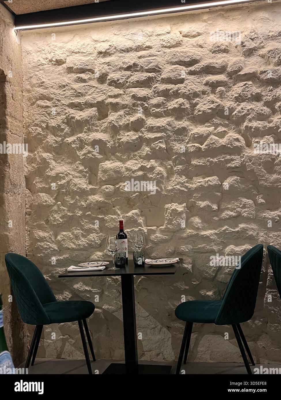 Intimate dining corner with a small table set for two against a textured white stone wall in Alicante, Spain. Includes wine, glasses, - Smartphone Captured Stock Image