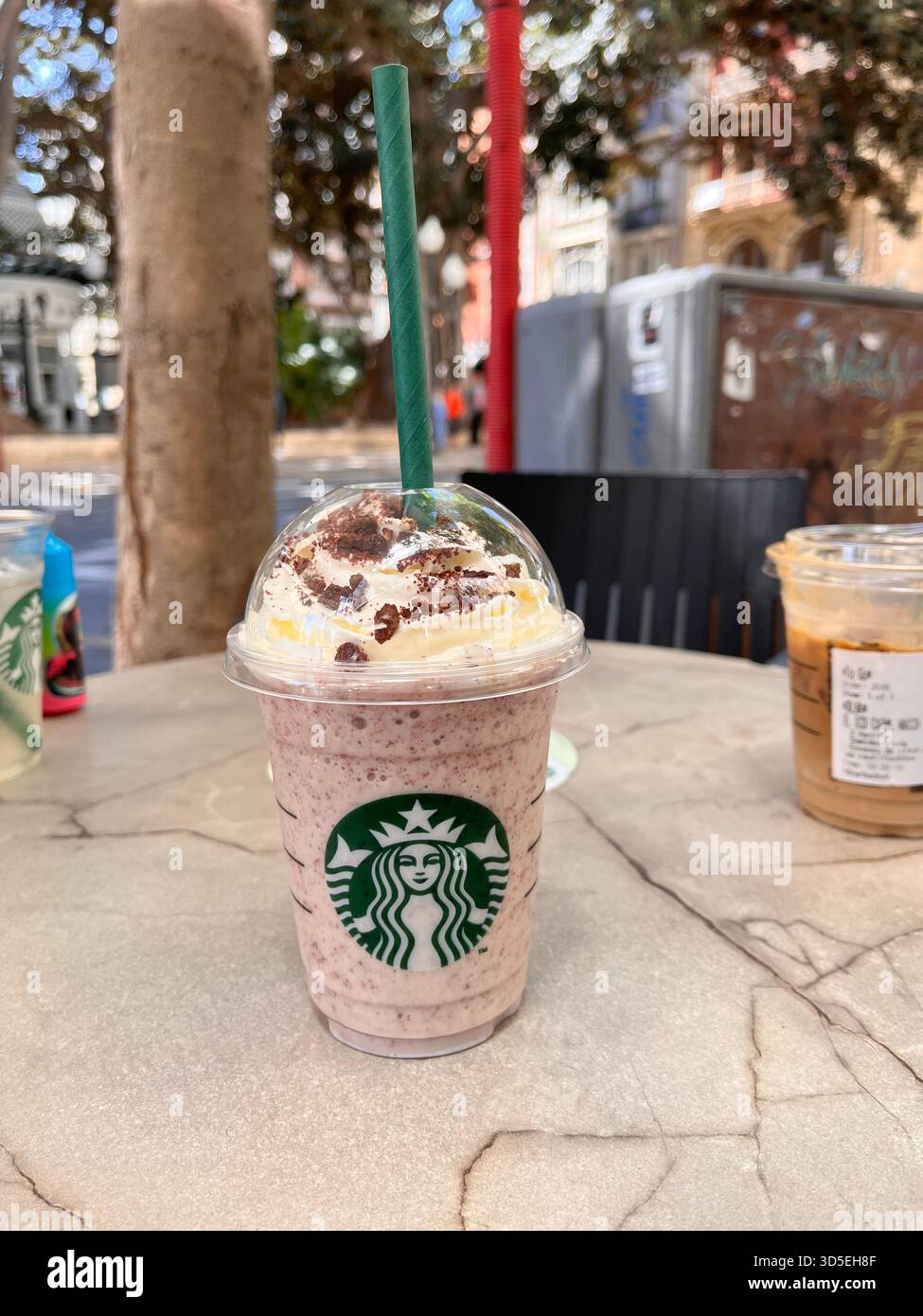 Cold Starbucks frappuccino resting on a sunlit table outdoors in Alicante, Spain. A refreshing summer moment captured in a Mediterranea - Smartphone Captured Stock Image