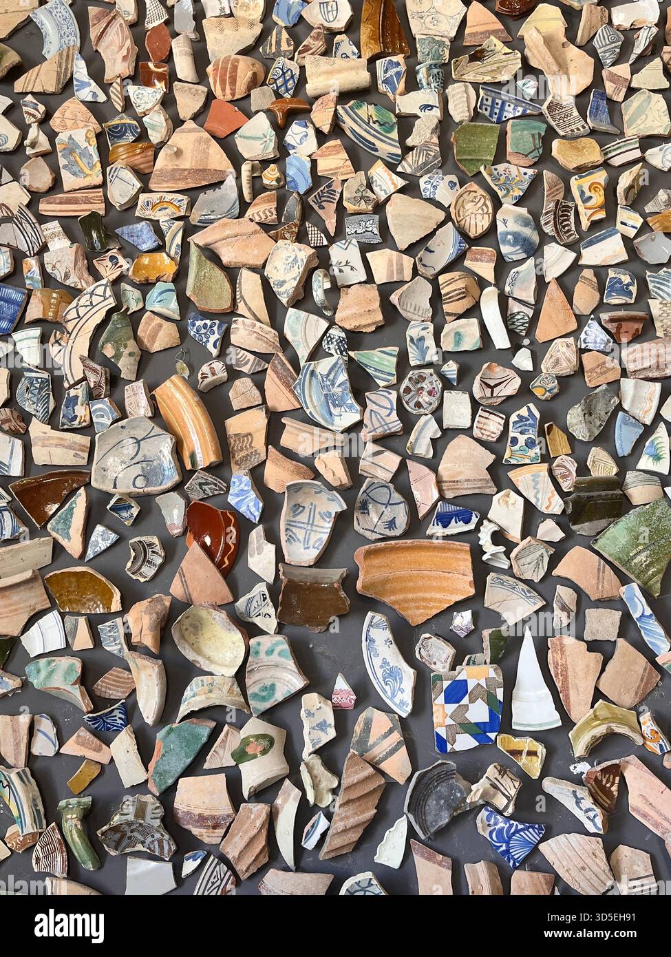 Detailed close-up of a textured mosaic wall created from colorful broken ceramics and pottery fragments in Alicante, Spain. - Smartphone Captured Stock Image