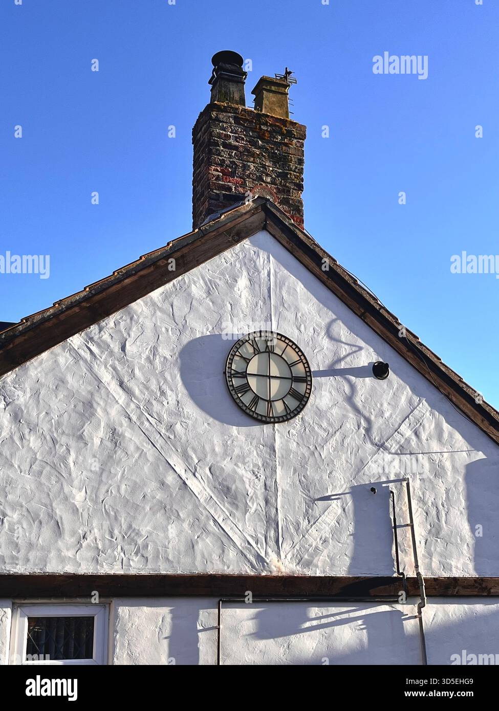 A charming white-plastered building with a round wall-mounted clock and a brick chimney, set against a clear blue sky in Alicante, Spain. - Smartphone Captured Stock Image