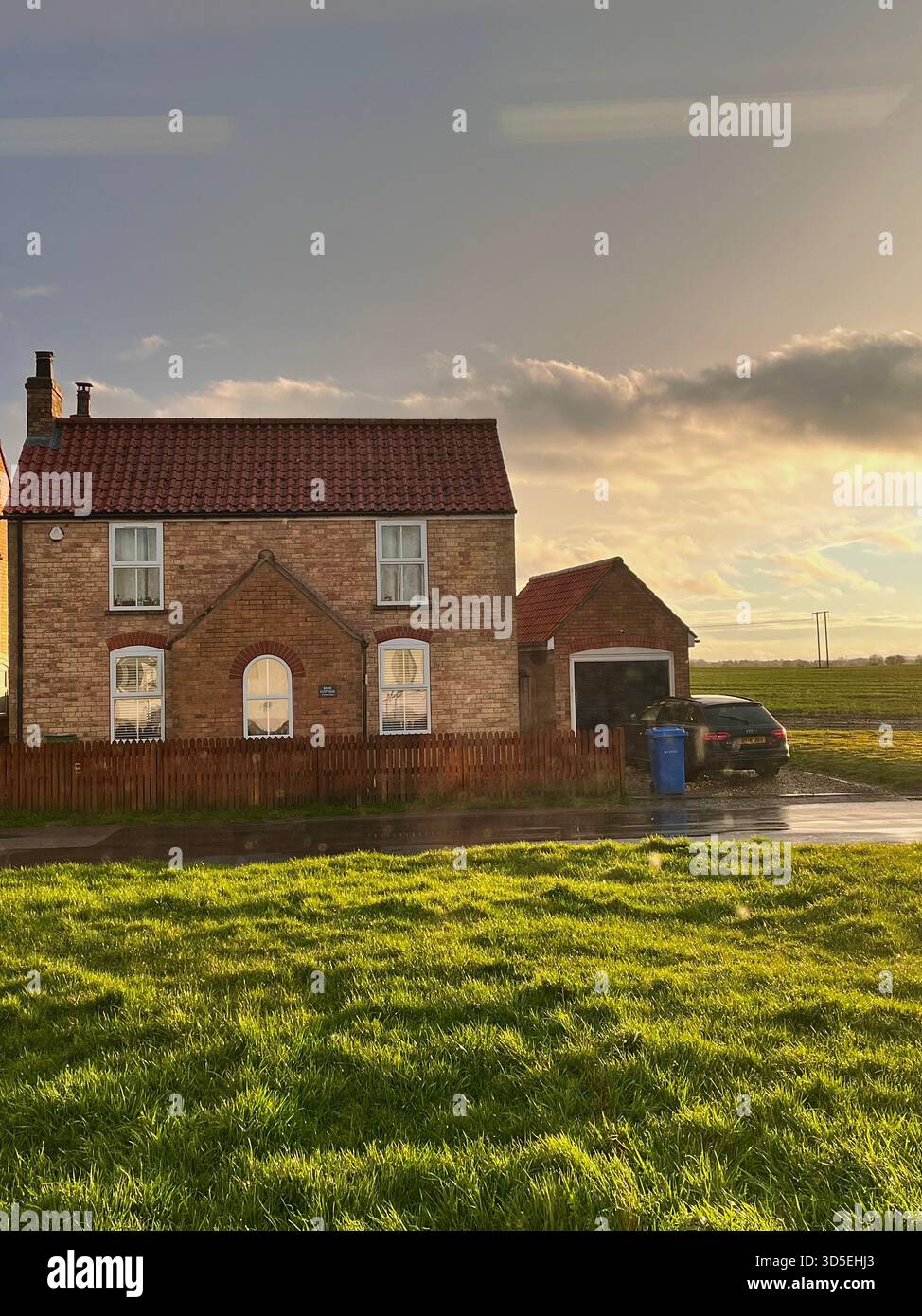 A cozy brick home with a tiled roof surrounded by green grass and illuminated by warm evening sunlight. Captured in Alicante, Spain, - Smartphone Captured Stock Image