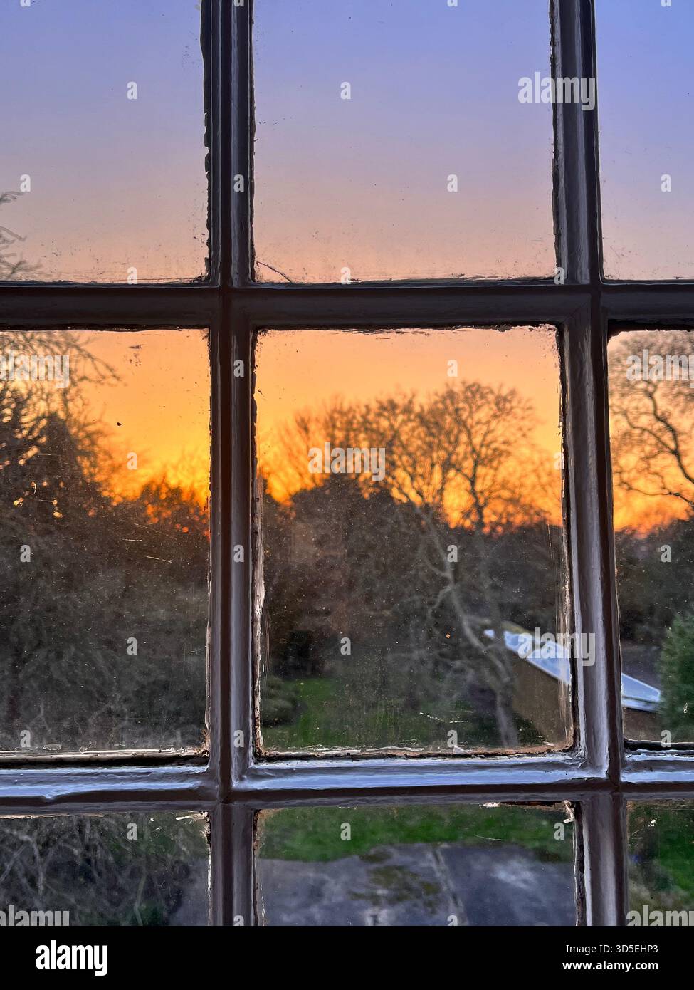 A rustic window with visible aging and a sunset sky reflected in the glass. Taken in Alicante, Spain, highlighting warmth, nostalgia, - Smartphone Captured Stock Image